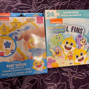 May include: A set of two Baby Shark themed toys. The first is a 9-piece finger paint set with a blue, yellow, and orange color scheme. The second is a 24-piece shaped puzzle featuring Baby Shark and friends.