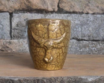 May include: A gold ceramic mug with a textured surface and a raised bull head design.