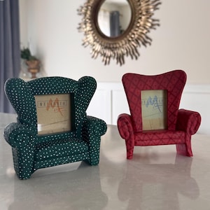 May include: Two miniature chair-shaped picture frames. One is dark green with white polka dots, the other is red with a diamond pattern. Both have a small rectangular space for a photo.