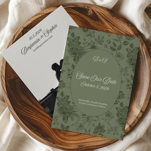 May include: Two wedding announcement cards on a wooden plate. One card is white with the names "Benjamin & Sophie" and the date "10.5.2026". The other card is green with floral designs and the text "Save Our Date October 5. 2026".