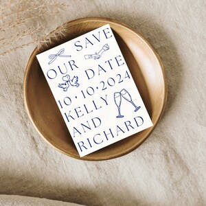 Pode incluir: Cart&atilde;o de guardar a data com tinta azul, apresentando um la&ccedil;o, dois p&aacute;ssaros e ta&ccedil;as de champanhe. O texto diz "Save Our Date 10.10.2024 Kelly and Richard".