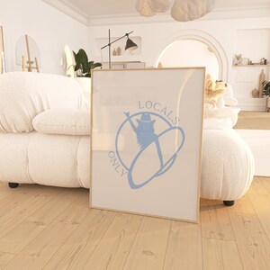 May include: A framed print with a light blue design of a woman wearing a cowboy hat and holding a surfboard. The text "LOCALS ONLY" is written in a circle around the woman.