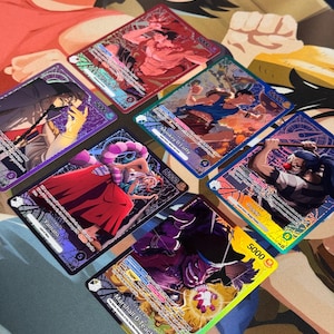 Op de afbeelding: Een verzameling van acht kleurrijke ruilkaarten met anime-personages. Elke kaart toont een unieke illustratie met namen en waarden. De kaarten zijn gerangschikt op een patroon, met levendige kunstwerken en gedetailleerde ontwerpen.