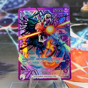 Puede incluir: Una carta coleccionable de One Piece de color morado que muestra al personaje Kaido en forma de dragón. La carta incluye el texto 'LEADER Kaido', '5000' de poder, '5' de vida y mecánicas de juego como 'When Attacking' y 'DON!!-1'.