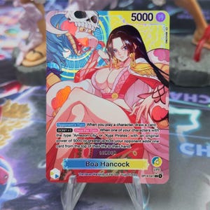 Può includere: Carta collezionabile con Boa Hancock della serie "One Piece". La carta presenta un design colorato con un ritratto del personaggio in un abito rosso e bianco. Testo con istruzioni di gioco e un potere di 5000.