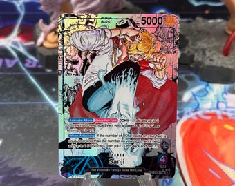 May include: A holographic trading card featuring the character Sanji from the One Piece series. The card has a colorful design with the number 5000 in the upper right corner. The card text includes the words "Activate: Main" and "When Attacking".