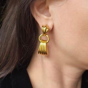 May include: Gold tone dangle earrings with a layered, fan-shaped design and a ring detail.