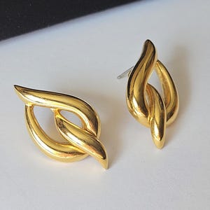 May include: A pair of gold-toned earrings with a twisted, leaf-like design. The earrings are made of metal and have a polished finish.
