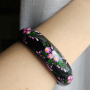 Könnte beinhalten: Schwarzes Bangel-Armband mit einem floralen Design, das in Pink und Grün bemalt ist.