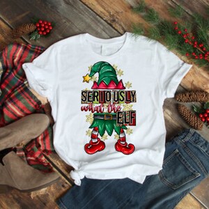 May include: White t-shirt with a green elf illustration and the text "SERIOUSLY what the ELF" in red, black, and gold lettering.