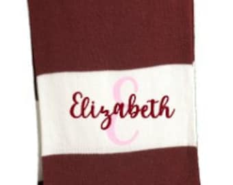 May include: Three personalized scarves with fringe. One is red, white, and black with "Addison" embroidered. Another is black and gray with "CBA" monogrammed. The third is burgundy and white with "Elizabeth" embroidered.
