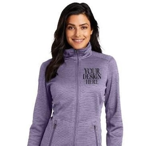 May include: A lavender zip-up jacket with a high collar and two front pockets. The jacket has the text "YOUR DESIGN HERE" printed on the chest. The model is wearing dark blue jeans.