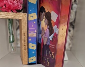 May include: Two paperback books on a shelf. The book on the left is blue and purple with gold stars and envelopes. The book on the right is red and purple with gold stars and the text "REUNITED BY LOVE? LESS VS".