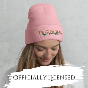 May include: A light pink beanie with the text "THE GUARDIAN layer of monsters" embroidered in gold and green. The words "OFFICIALLY LICENSED" are below the beanie.