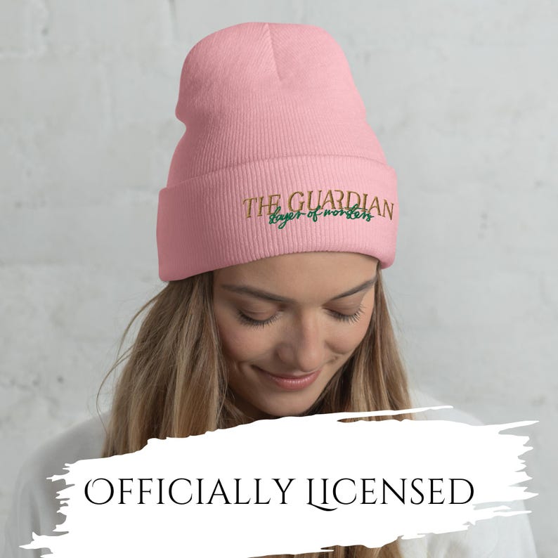 May include: A light pink beanie with the text "THE GUARDIAN layer of monsters" embroidered in gold and green. The words "OFFICIALLY LICENSED" are below the beanie.