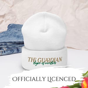 May include: A white beanie with the text "THE GUARDIAN slayer of monsters" in brown and green. The beanie is made of a soft material and is suitable for cold weather. The text "OFFICIALLY LICENSED" is also visible.