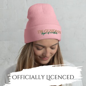 May include: A light pink beanie with the text "THE GUARDIAN slayer of words" embroidered in gold and green. The words "OFFICIALLY LICENSED" are printed below the beanie.