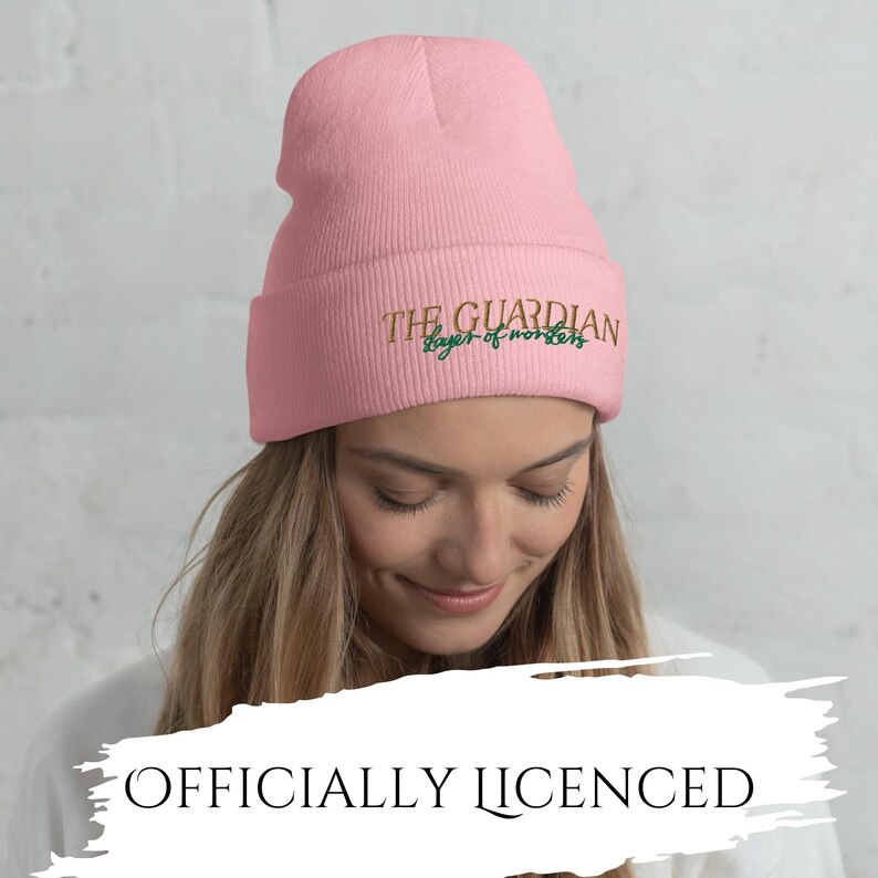 May include: A light pink beanie with the text "THE GUARDIAN slayer of words" embroidered in gold and green. The words "OFFICIALLY LICENSED" are printed below the beanie.