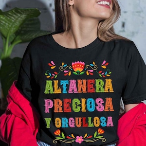 Puede incluir: Camiseta negra con un diseño floral colorido y el texto "ALTANERA PRECIOSA Y ORGULLOSA" en una fuente arcoíris.