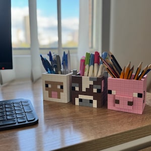 以下が含まれることがあります： Minecraftのキャラクターの形をしたカラフルな鉛筆立て3つ。鉛筆立てはプラスチック製で、ブタ、牛、羊が描かれています。鉛筆立てには、さまざまな色のペンと鉛筆が入っています。