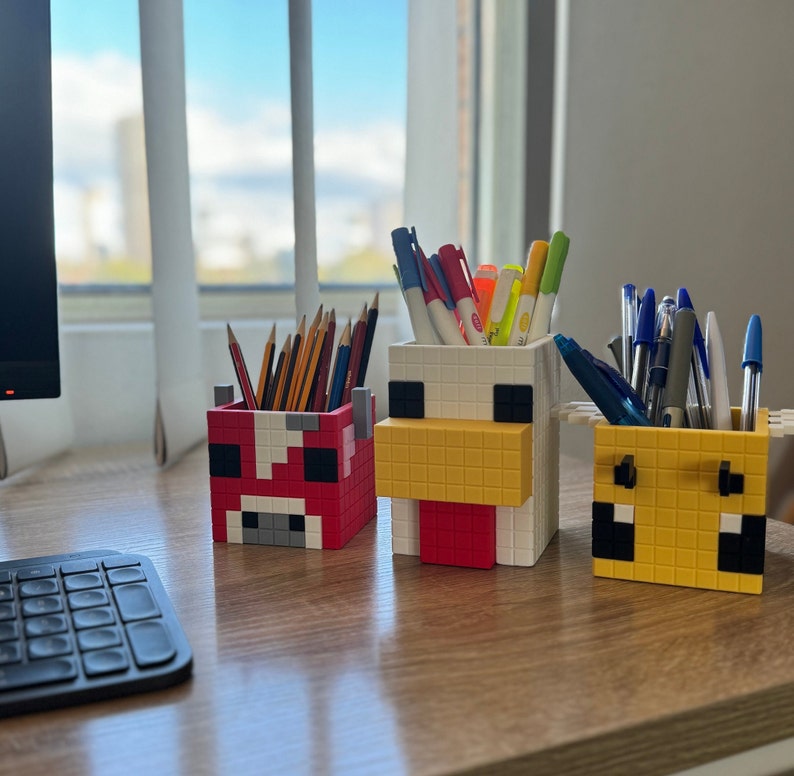 Pode incluir: Tr&ecirc;s porta-l&aacute;pis coloridos em forma de personagens do Minecraft. Os porta-l&aacute;pis s&atilde;o feitos de pl&aacute;stico e t&ecirc;m um design pixelado. Os personagens s&atilde;o uma vaca, uma galinha e um porco. Os porta-l&aacute;pis est&atilde;o cheios de canetas e l&aacute;pis.
