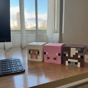 May include: Three Minecraft-themed block figures, a white sheep, a pink pig, and a brown cow, are lined up on a wooden surface.