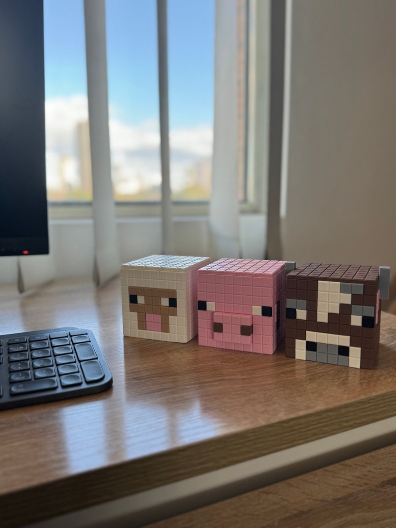 May include: Three Minecraft-themed block figures, a white sheep, a pink pig, and a brown cow, are lined up on a wooden surface.