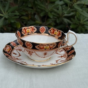 Puede incluir: Un juego de taza y platillo de té vintage con un patrón floral negro, rojo y dorado.