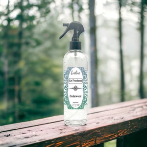 May include: A clear glass bottle with a black spray nozzle and a label that says "Eveline Air Freshener Cedarwood". The bottle is sitting on a wooden surface.