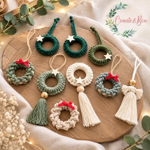 May include: A collection of handmade macrame ornaments featuring small circular wreaths in shades of green, cream, and white. Several ornaments include wooden star accents, gold-toned beads, red ribbon bows, and hanging tassels. The text Connie & Bea is visible.