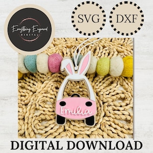 Könnte beinhalten: Ein rosa, auto-förmiger Ornament mit Hasenohren, dem Namen "Emilia" in weißer Schrift und schwarzen Rädern. Das Bild enthält den Text "SVG" und "DXF" in Kreisen sowie "Everything Engraved DIGITAL" in einem kreisförmigen Logo. Unten steht "DIGITAL DOWNLOAD".