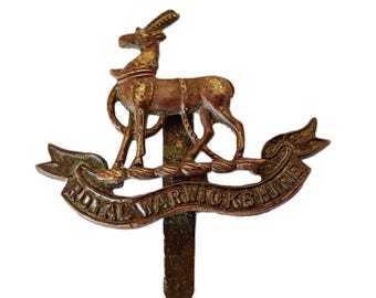 May include: A bronze cap badge with a depiction of a deer and the text "Royal Warwickshire" on a ribbon.