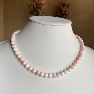 May include: A delicate necklace made of pink and white shell beads. The beads are round and smooth, and the necklace is strung on a thin cord.