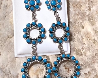 May include: A pair of dangle earrings featuring three turquoise circles and a turquoise flower at the top. The earrings are silver and have a southwestern style.