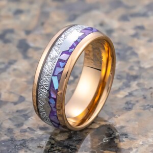 Puede incluir: Un anillo de carburo de tungsteno de oro rosa con una incrustaci&oacute;n p&uacute;rpura y blanca. La incrustaci&oacute;n est&aacute; hecha de meteorito triturado y n&aacute;car.