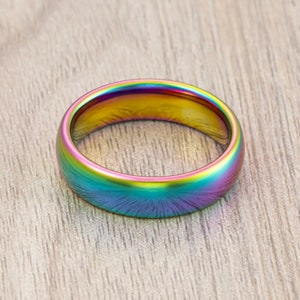 May include: A rainbow iridescent ring made of tungsten carbide. The ring has a polished finish and a rounded shape.