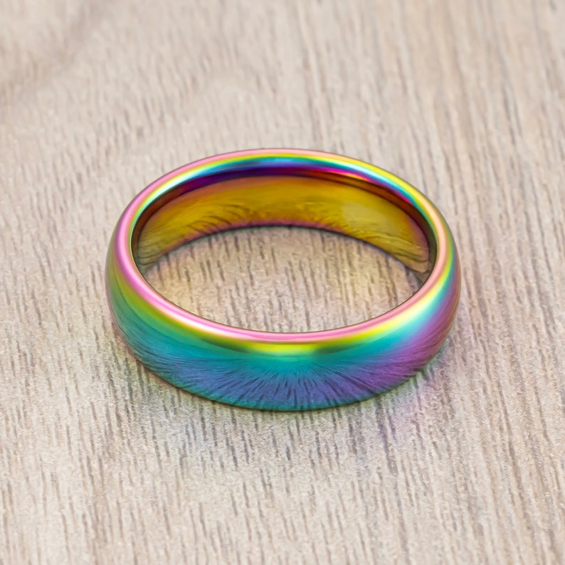 May include: A rainbow iridescent ring made of tungsten carbide. The ring has a polished finish and a rounded shape.