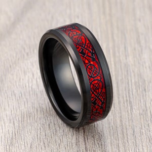 May include: Black tungsten carbide ring with a red Celtic knot design.