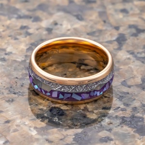 Puede incluir: Un anillo de oro y plata con una incrustaci&oacute;n de color p&uacute;rpura y blanco. El anillo tiene una banda texturizada y un acabado pulido.