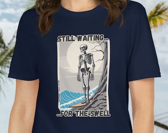 May include: A navy blue t-shirt with a graphic of a skeleton standing on a surfboard with the text "STILL WAITING... ...FOR THE SWELL".