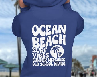 May include: A royal blue hoodie with white text on the back that reads "Ocean Beach Surf Vibes Summer Memories Old School Riding" with a palm tree graphic. The hoodie is a solid color and has a hood.