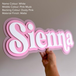 May include: A layered wall sign featuring the name Sienna in white matte lettering, set against a pink musk middle layer and a dusty pink backing layer. The text reads: Name Colour: White, Middle Colour: Pink Musk, Backing Colour: Dusty Pink, Material Finish: Matte.