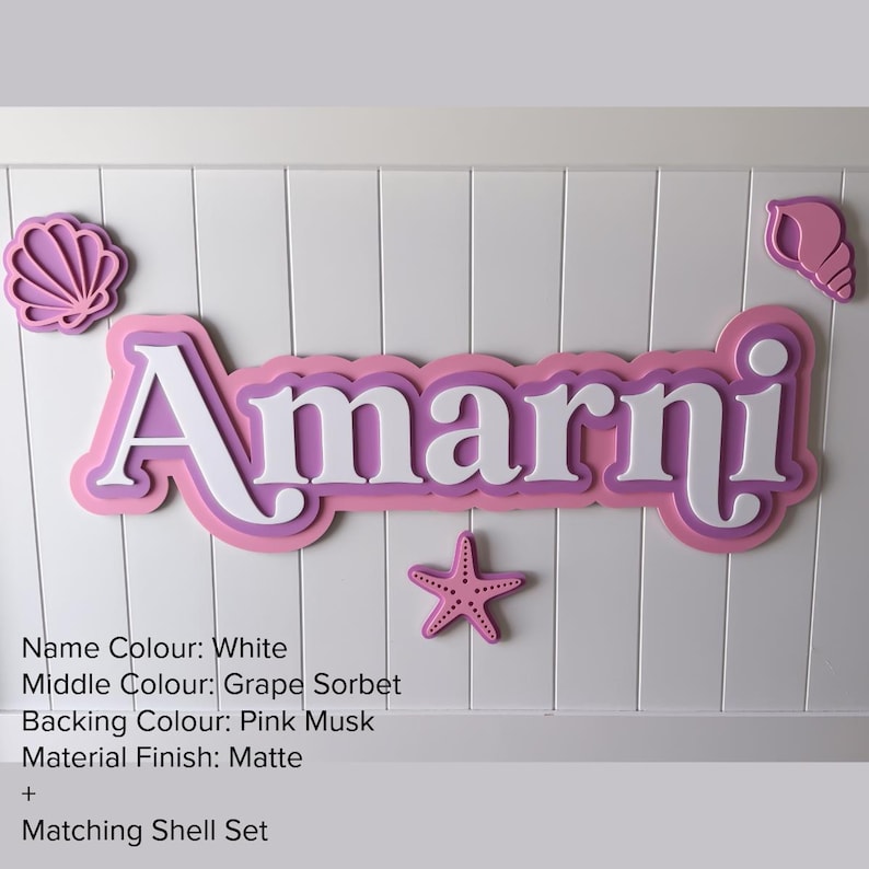 May include: A custom name sign featuring the name Amarni in white letters with a grape sorbet middle layer and a pink musk backing. The sign includes decorative shell and starfish accents in matching colors, all with a matte finish.