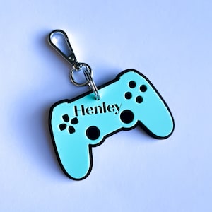 May include: A light blue plastic keychain shaped like a video game controller with the name "Henley" printed on it. The keychain has a silver metal ring and clip.