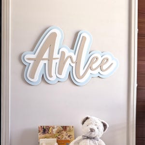 May include: A three-dimensional wooden name sign with the name "Arlee" in a cursive font. The sign is painted in shades of blue and beige.