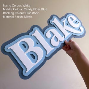 May include: A custom name sign featuring the name Blake in white, layered over a candy floss blue middle section and a bluestone backing. The sign has a matte finish and includes the text: Name Colour: White, Middle Colour: Candy Floss Blue, Backing Colour: Bluestone, Material Finish: Matte.