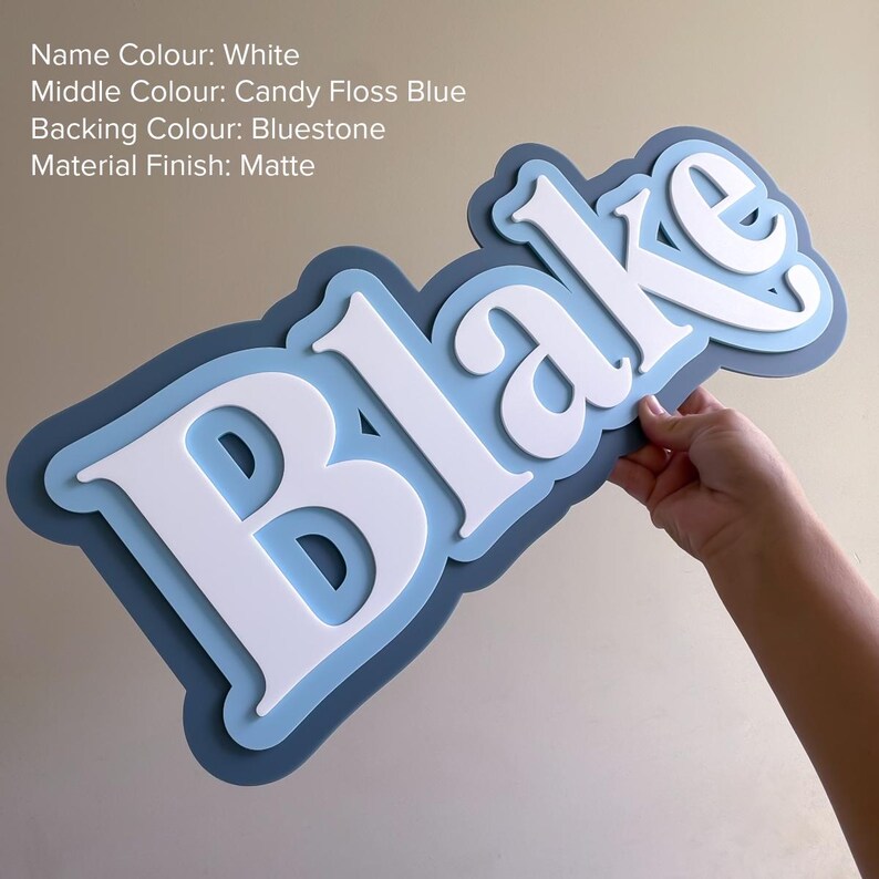 May include: A custom name sign featuring the name Blake in white, layered over a candy floss blue middle section and a bluestone backing. The sign has a matte finish and includes the text: Name Colour: White, Middle Colour: Candy Floss Blue, Backing Colour: Bluestone, Material Finish: Matte.