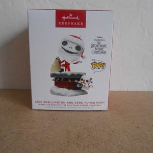 May include: A Hallmark Keepsake box featuring a Jack Skellington and Zero Funko Pop! figure from Disney's The Nightmare Before Christmas. The box is white with red accents and includes the text "Hallmark Keepsake" and "POP!".