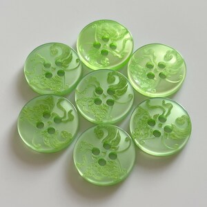 May include: A set of seven round, translucent light green buttons arranged in a cluster. Each button features a four-hole centre and an embossed, swirling, organic pattern that resembles flowing hair or stylised flames across the surface.