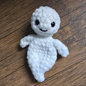 May include: A white crocheted ghost with black eyes and a smiling mouth. The ghost has a fluffy texture and is a handmade toy.
